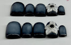 Set of black nail tips with silver flower designs on a light gray background