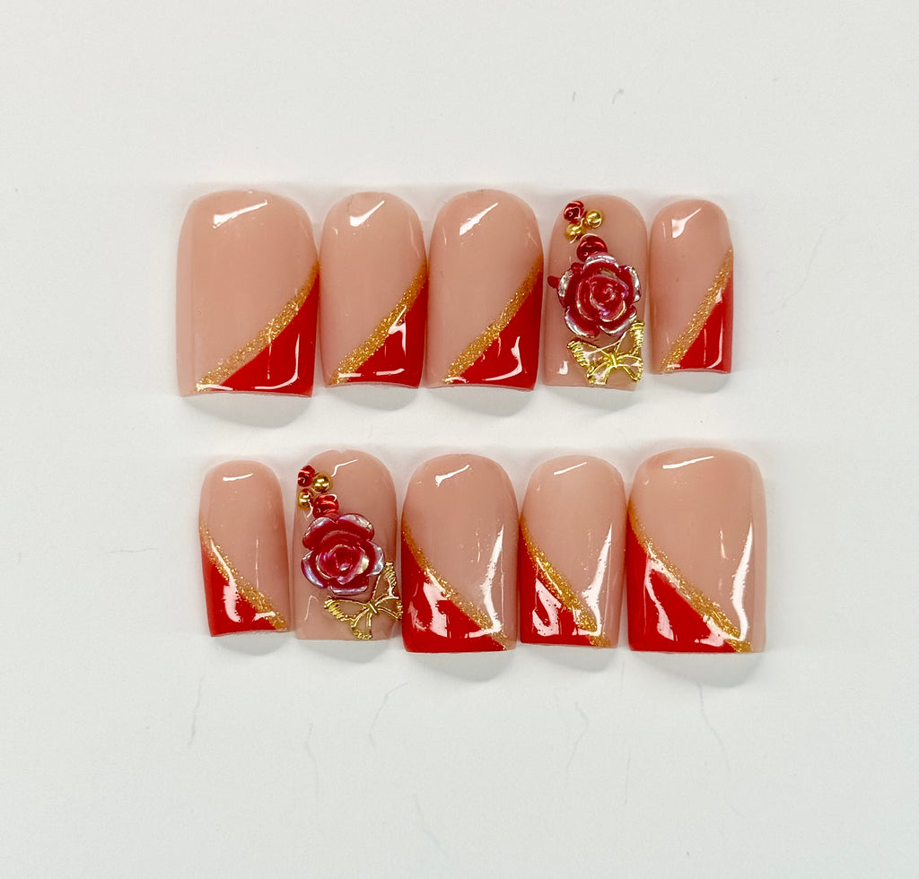 Nail art with red and gold designs on beige nails against a white background