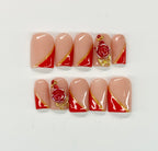Nail art with red and gold designs on beige nails against a white background