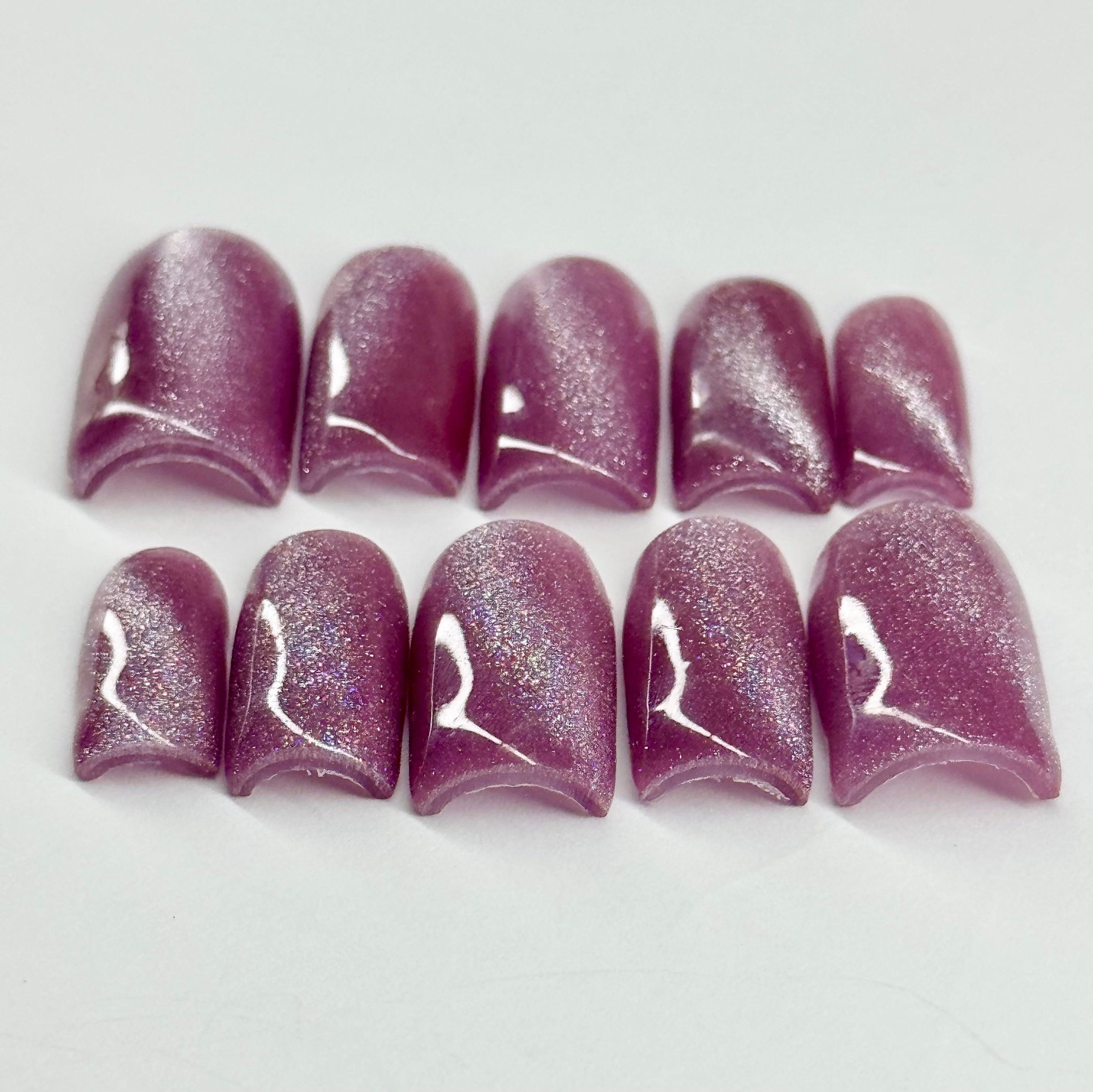 Set of purple glittery cat eye nail tips on a white background