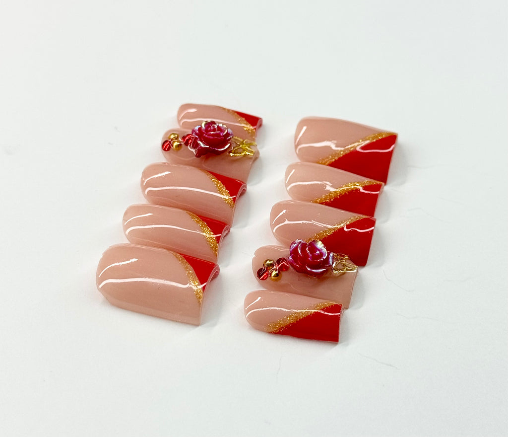 Decorative nail art with red, gold, and pink design on a white background