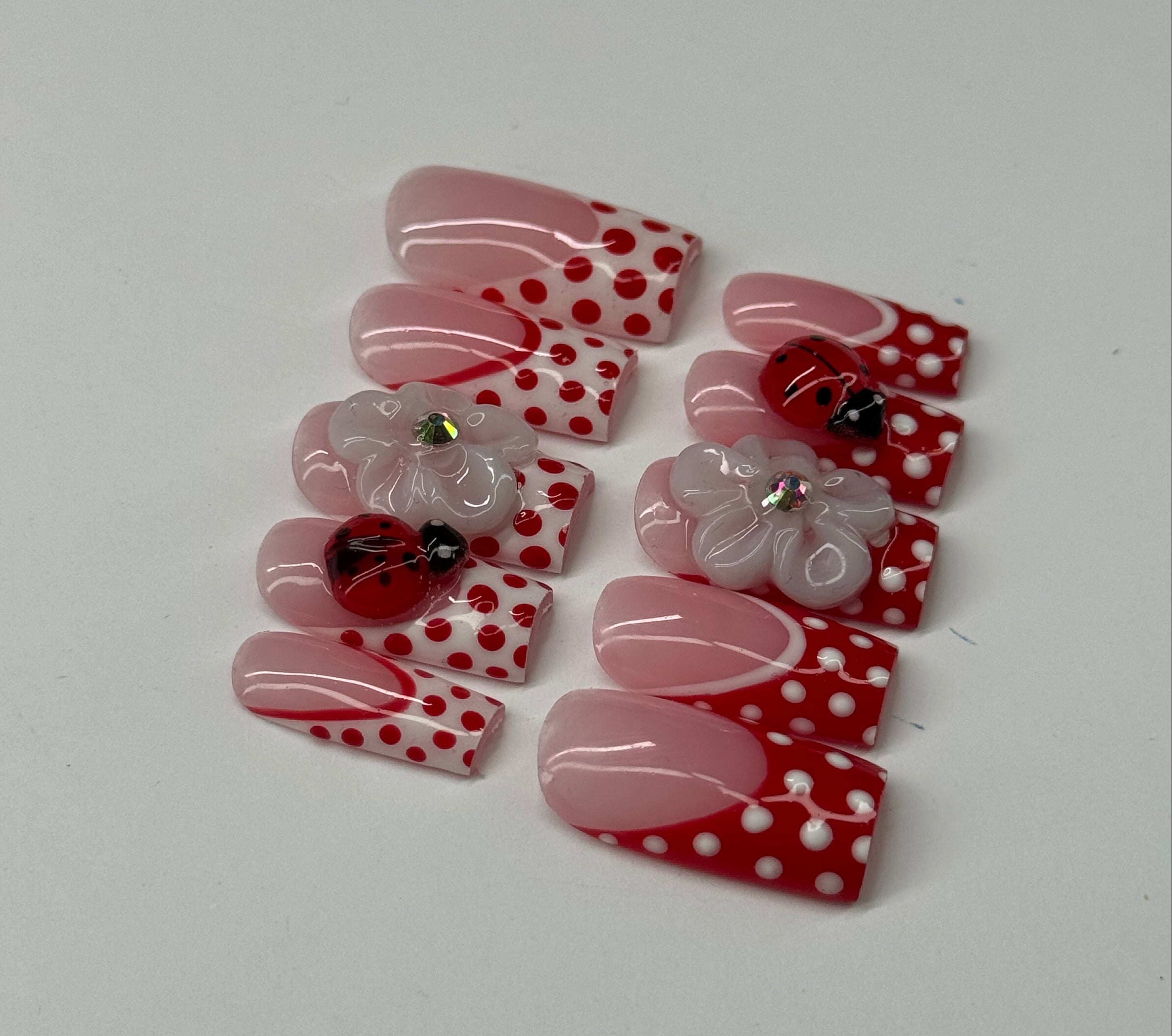 Set of artificial nails with red and white polka dot design on a light gray background
