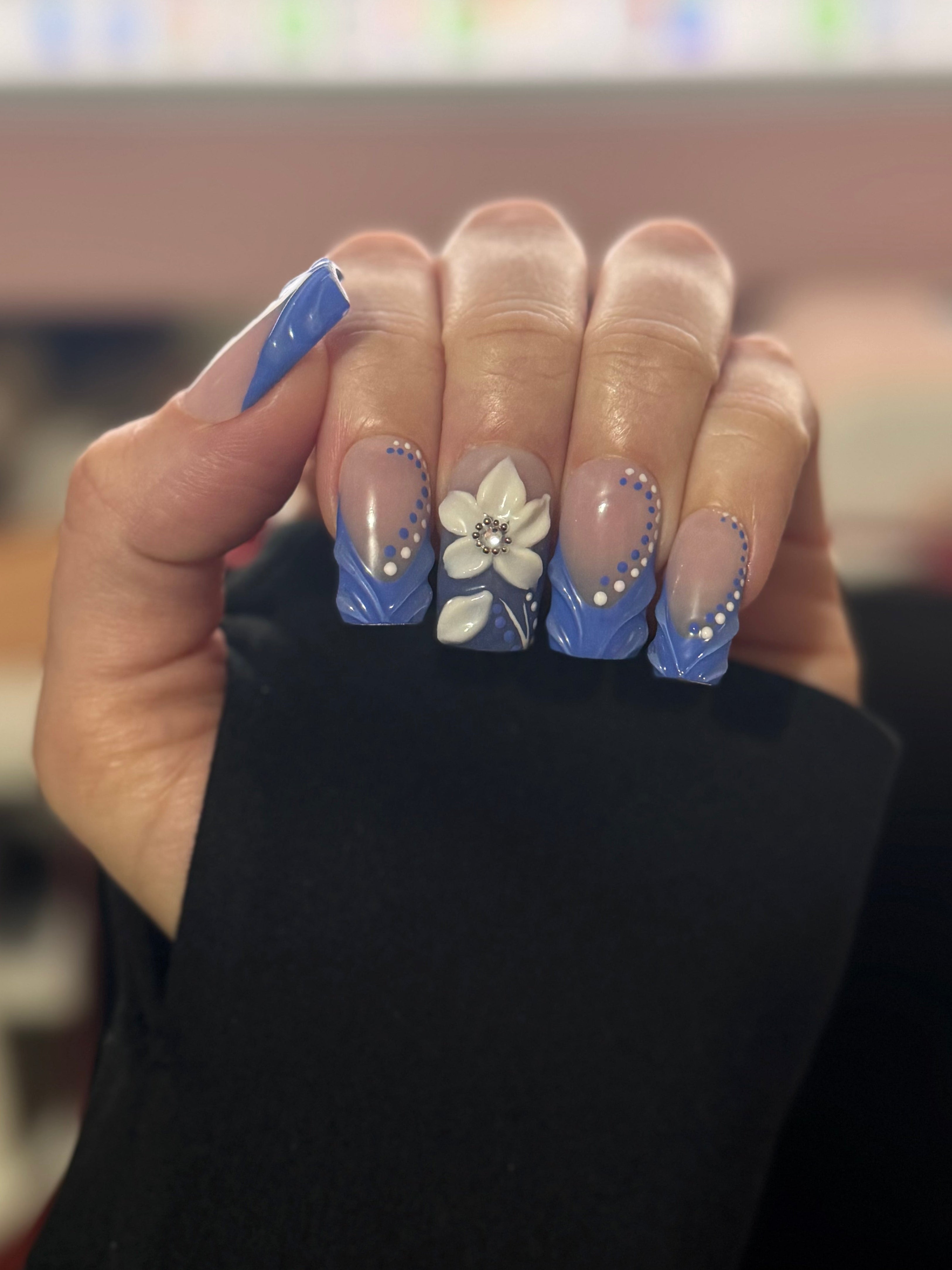 Realistic Hand with blue and white floral nail art holding a blue nail file.