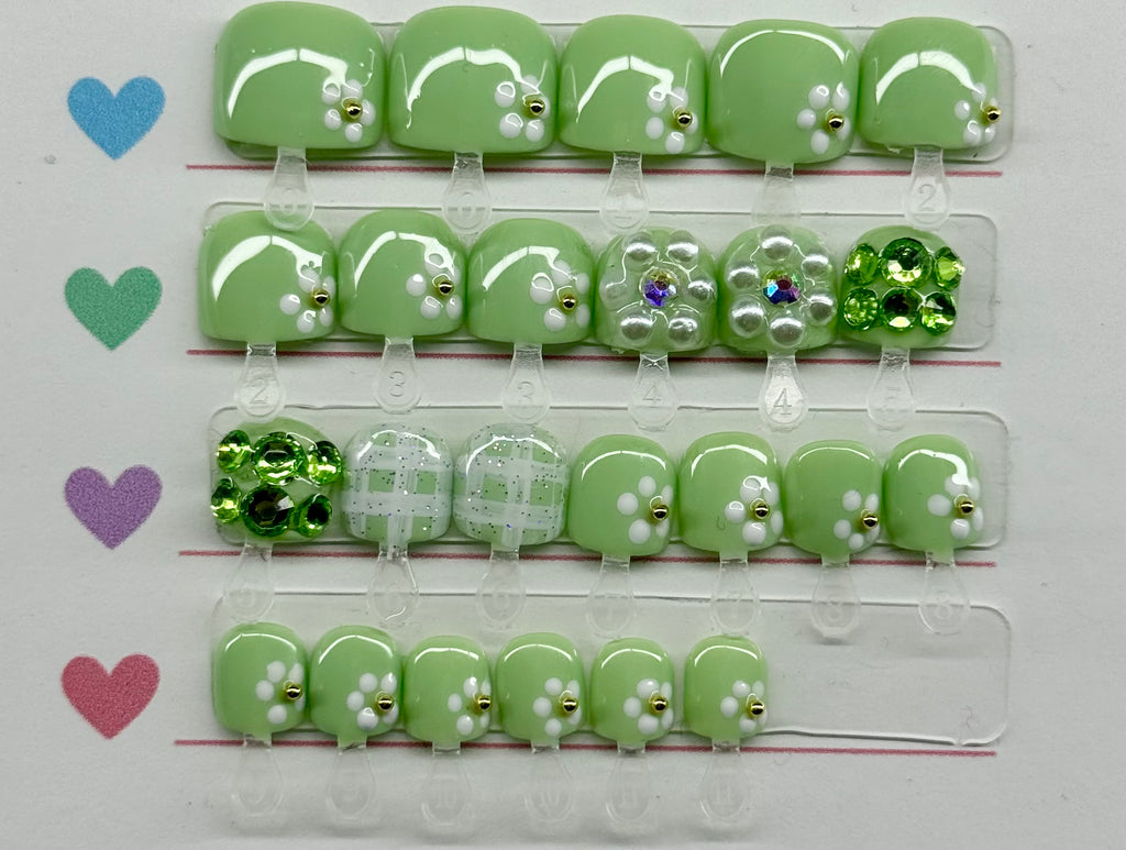Set of pastel green nail art decorations with various gemstones on a clear plastic strip.